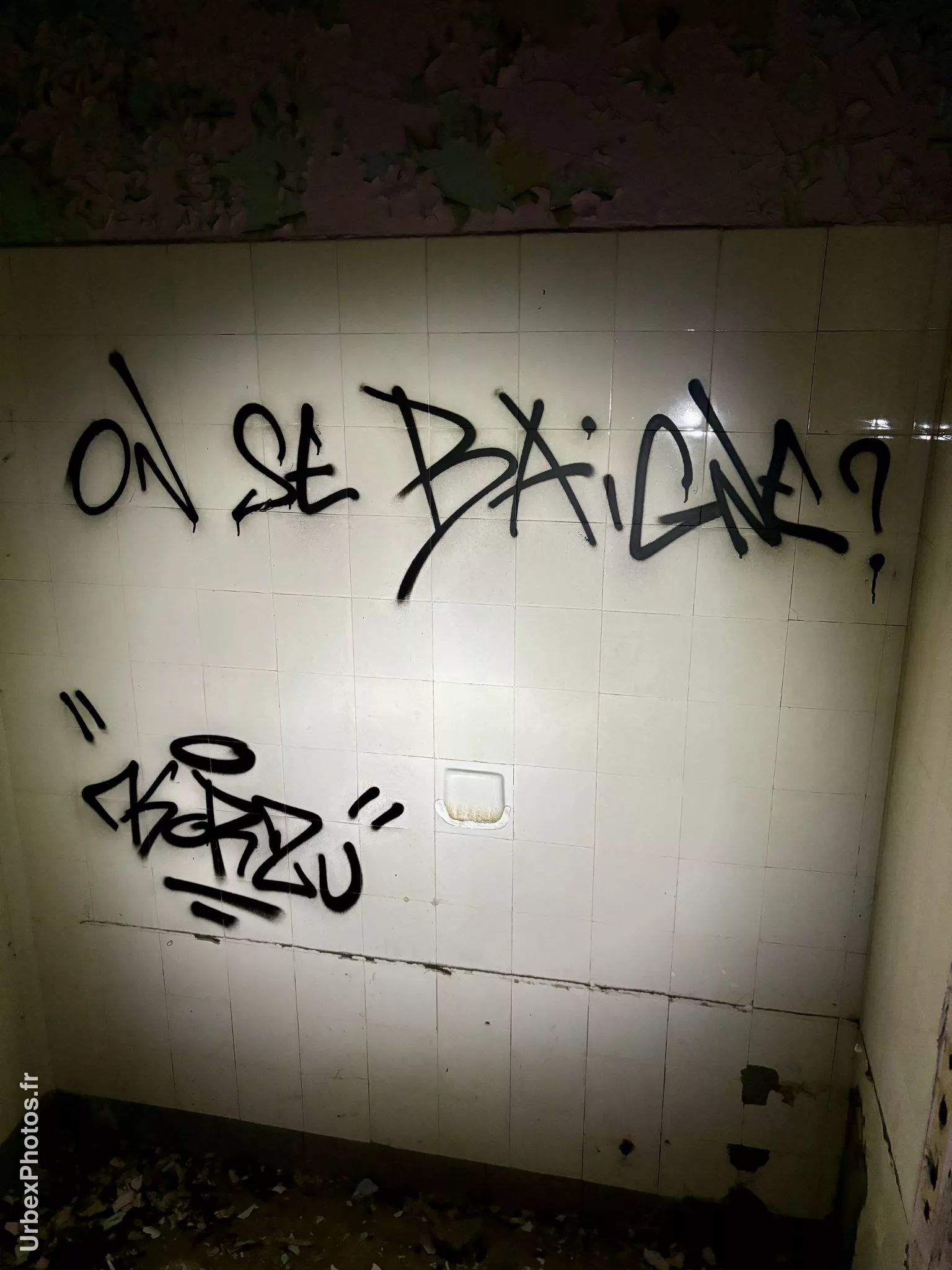 Message "On se baigne ?" sur un mur carrelé