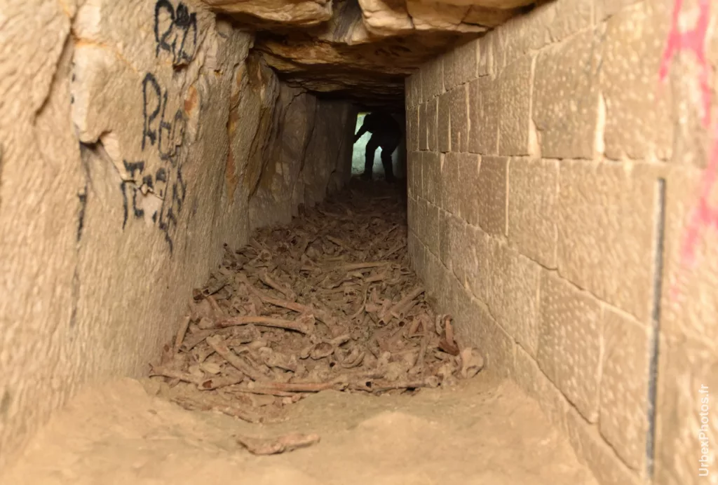 Photo urbex d'une galerie recouverte d'ossements et quelqu'un marchant dessus dans les catacombes interdites de Paris
