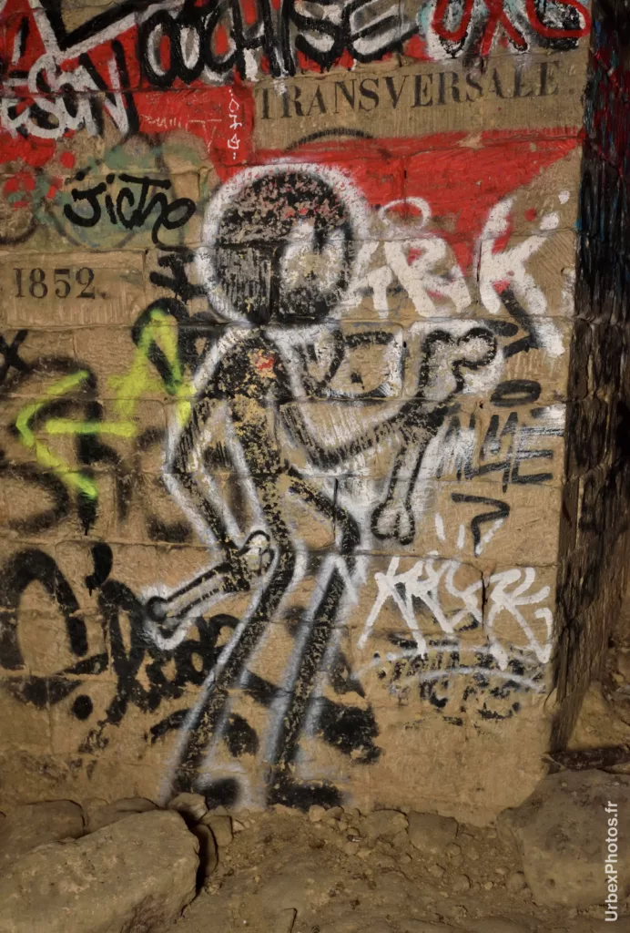 Photo urbex du graffiti d'un stickman avec un os à chaque main dans les catacombes interdites de Paris